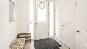Un couloir avec un banc, une porte dotée d’un panneau en verre et un paillasson.