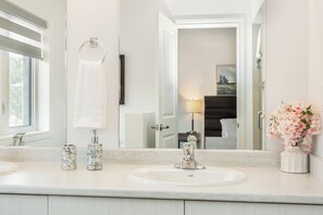Un baño con lavamanos blanco, un espejo y una ventana.