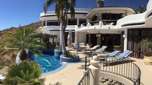 Un resort con piscina, sillas de descanso y un edificio grande con múltiples ventanas y balcones.
