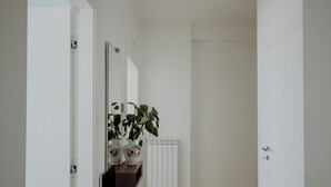 Ein Flur mit weißen Wänden, einem Heizkörper und einem Topfpflanzen auf einem Regal.