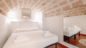 Ein Schlafzimmer mit Ziegeldecke, einem großen Spiegel, einem Bett mit weißer Bettwäsche und einem kleinen Teppich auf dem Boden.