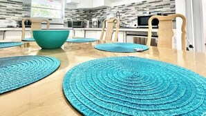 Una cocina moderna con armarios blancos, un cuenco verde azulado y una mesa de comedor de madera con individuales azules.