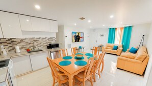 Una cocina moderna con armarios blancos, salpicadero de azulejos y una zona de comedor con mesa y sillas de madera.