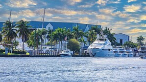 Un puerto deportivo con un yate grande amarrado, palmeras y un edificio con techo azul.