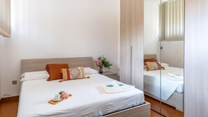 Quarto de hotel com uma cama grande, uma mesa de cabeceira, um espelho e uma janela com persianas.