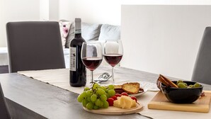 Uma mesa de jantar com uma garrafa de vinho, duas taças de vinho tinto, um bowl de azeitonas, um prato com queijo e uvas, e fatias de pão.