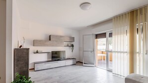 Uma sala de estar espaçosa com televisão de tela plana, estantes embutidas e uma porta de vidro deslizante que dá para uma área externa.
