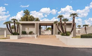 A modern building with a flat roof, a central entrance with steps, and palm trees around.