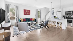 Una sala de estar moderna con sofá, mesa de centro y televisor. Cuenta con una zona de cocina con microondas y estufa.