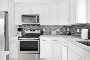 Una cocina moderna con armarios blancos, horno de acero inoxidable, microondas y salpicadero de azulejos.