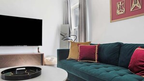 Una sala de estar con un sofá color turquesa, un televisor de pantalla plana, una mesa redonda y una obra de arte enmarcada en la pared.