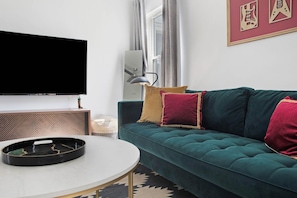 Una sala de estar con un sofá verde azulado, un televisor de pantalla plana, una mesa de centro y un cuadro enmarcado en la pared.