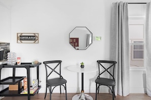 Una habitación con una mesa redonda, dos sillas, un letrero de cafetería, un espejo y una ventana con cortinas.
