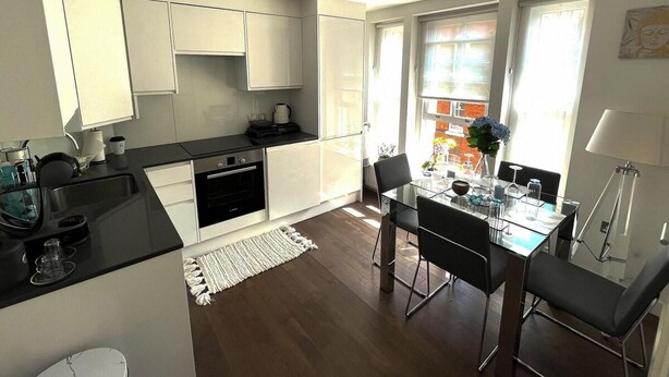 A modern kitchen with white cabinets, a black countertop, and a dining area with a glass table and chairs. - Luxurious 2 Beds Flat in Mayfair on Oxford Street (London)