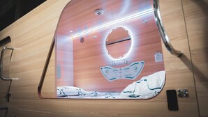 Une chambre moderne et compacte, avec un revêtement en bois, un miroir rond et un lit recouvert d’une couvre-lit à motifs.