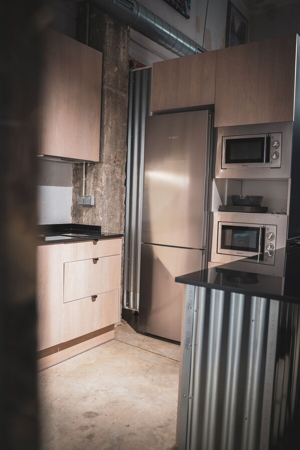 A compact kitchen with a stainless steel refrigerator, double microwave, and wooden cabinets. - Gallery Hostel Madrid (Madrid)