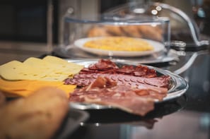 Un bufé con diversos alimentos, incluyendo queso, carnes y un recipiente tapado al fondo.