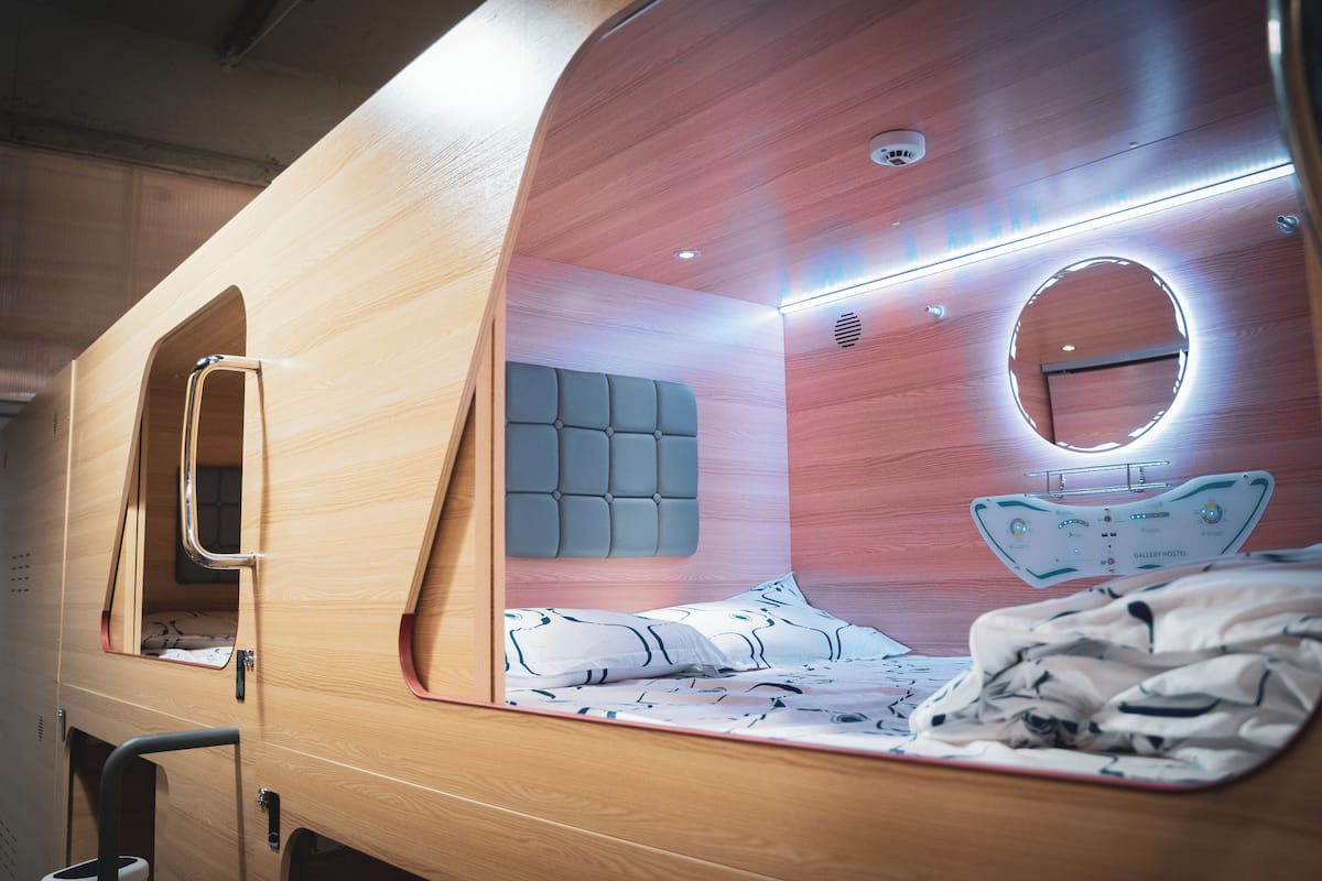 Une chambre moderne et compacte, avec un lit superposé, une petite fenêtre et un miroir rond accroché au mur.