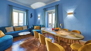 A room with a blue wall, a sofa, a dining table with chairs, and a window with curtains. - Spacious dwelling between Vatican and Center [3 bedrooms, 3 baths] (Roma)