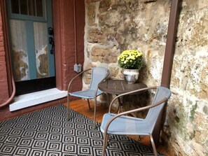 Eine rustikale Steinwand, ein Metalltisch mit zwei Stühlen, ein Blumentopf und ein gemustertes Teppich.