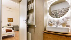 A hotel room with a bed, a bedside table, a nightstand, a wardrobe, and a bathroom with a sink and mirror. - Santa Patrizia a Chiaia Apartment - Terra (Naples)