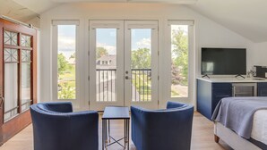 Een slaapkamer met een bed, een televisie, een bureau en een balkon met uitzicht op de omgeving.