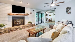 A living room with a fireplace, a ceiling fan, and a large window. - Marina Villa Condo at Lake Keowee w/ Fireplace (Salem)