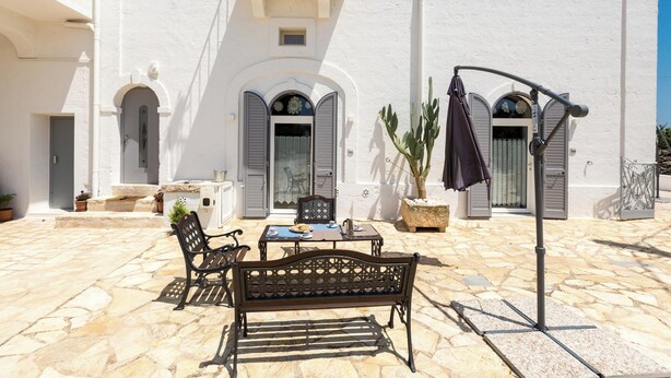 Un patio con suelo de piedra, un banco, una mesa y una planta en maceta.