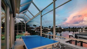 A ping pong table in a covered outdoor area with a view of a marina and boats.