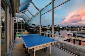 A ping pong table in a covered outdoor area with a view of a marina and boats. - Luxury Waterfront Villa with Heated Pool & Dock (Marco Island)