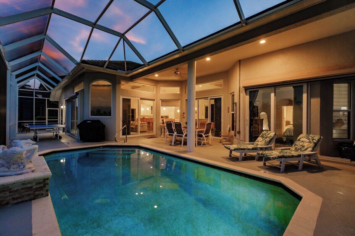 Una piscina con sillones de descanso y un patio cubierto.