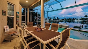 A covered outdoor dining area with a pool view, a dining table with chairs, and a sign indicating no diving. - Luxury Waterfront Villa with Heated Pool & Dock (Marco Island)