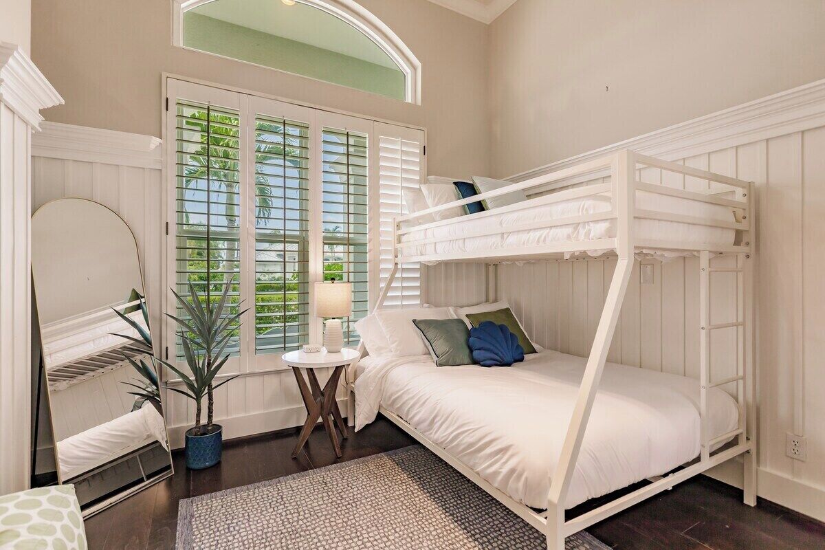 Une chambre avec un lit superposé, un miroir rond, une plante en pot et une fenêtre avec des stores.