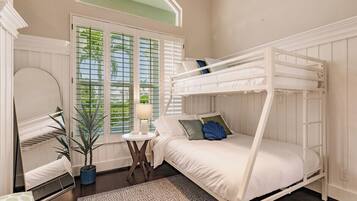 Une chambre avec un lit superposé, un miroir rond, une plante en pot et une fenêtre avec des stores.