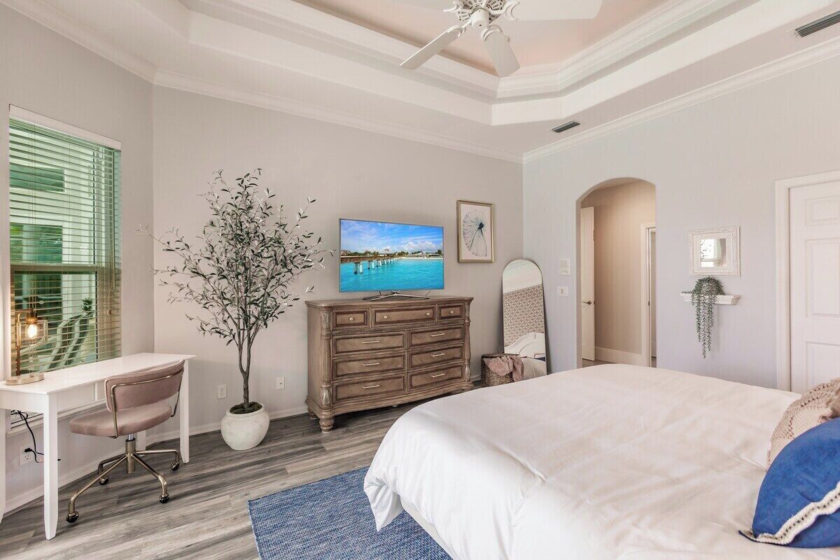Un dormitorio con cama, escritorio, silla, cómoda, televisor y planta en maceta.