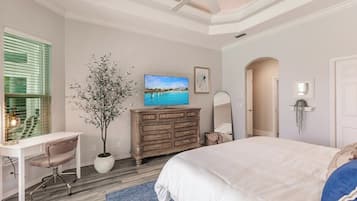 Un dormitorio con cama, escritorio, silla, cómoda, televisor y planta en maceta.