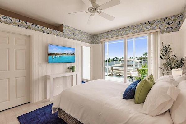 A bedroom with a large bed, a television, and a view of a pool and buildings through a sliding glass door.