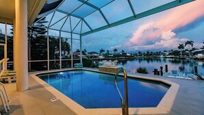 An indoor swimming pool with a glass ceiling, surrounded by palm trees and a view of a body of water. - Luxury Waterfront Villa with Heated Pool & Dock (Marco Island)