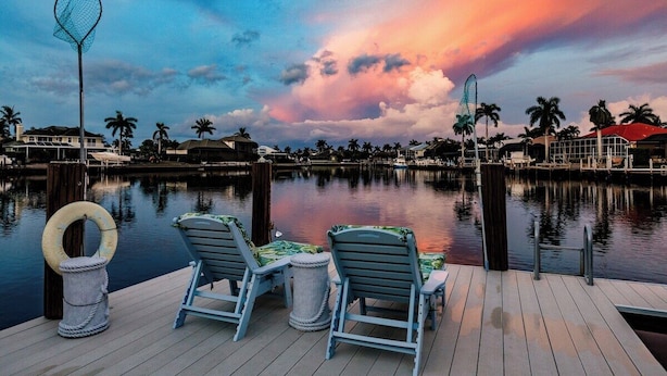 A waterfront deck with two lounge chairs, a netted structure, and a row of palm trees. - Luxury Waterfront Villa with Heated Pool & Dock (Marco Island)