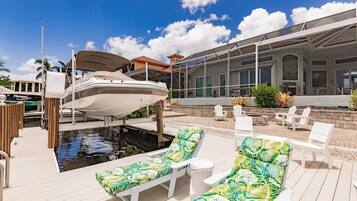 A marina with a boat docked, a pool area with lounge chairs, and a building with large windows.