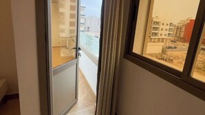 Un couloir avec une porte coulissante en verre donnant sur un balcon d’où l’on peut admirer des immeubles et une rue.