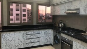 Une cuisine moderne avec des plans de travail en marbre, un lave-linge encastré et une vue sur un chantier de construction par de grandes fenêtres.