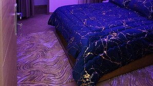 Een moderne slaapkamer met een groot bed, paars licht, een kroonluchter en uitzicht door een raam.