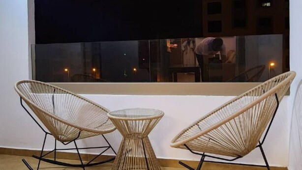 Een balkon met twee rieten schommelstoelen en een klein, rond tafeltje, met uitzicht op een stadsgezicht 's nachts.