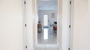 A hallway with a marble floor leading to a room with a door, a chair, and a table.
