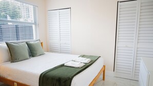A neatly made bed with a green blanket, white pillows, and folded towels.