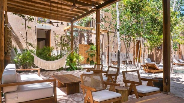 An outdoor seating area with wooden furniture and a hammock, surrounded by greenery and a pool. - 3BR Home in Gated Community | Rooftop Plunge Pool, Grill & Shared Poo (Tulum)