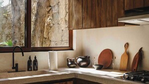 A kitchen with wooden cabinets, a window with a view of trees, and a stove. - 3BR Home in Gated Community | Rooftop Plunge Pool, Grill & Shared Poo (Tulum)