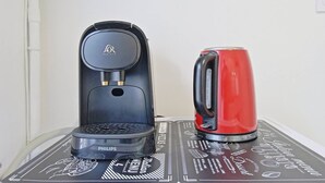 En sort Philips-kaffemaskine og en rød elkedel på et bord med en sort bordskåner med italienske menugrafik.