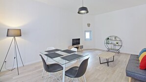 En moderne stue med et glasbord, sorte stole, en sofa, et fjernsyn og en gulvlampe.